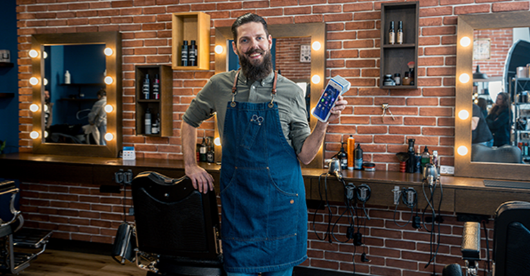 Lachender Barber im Barbershop hält ein myPOS Ultra Kartenterminal in die Kamera